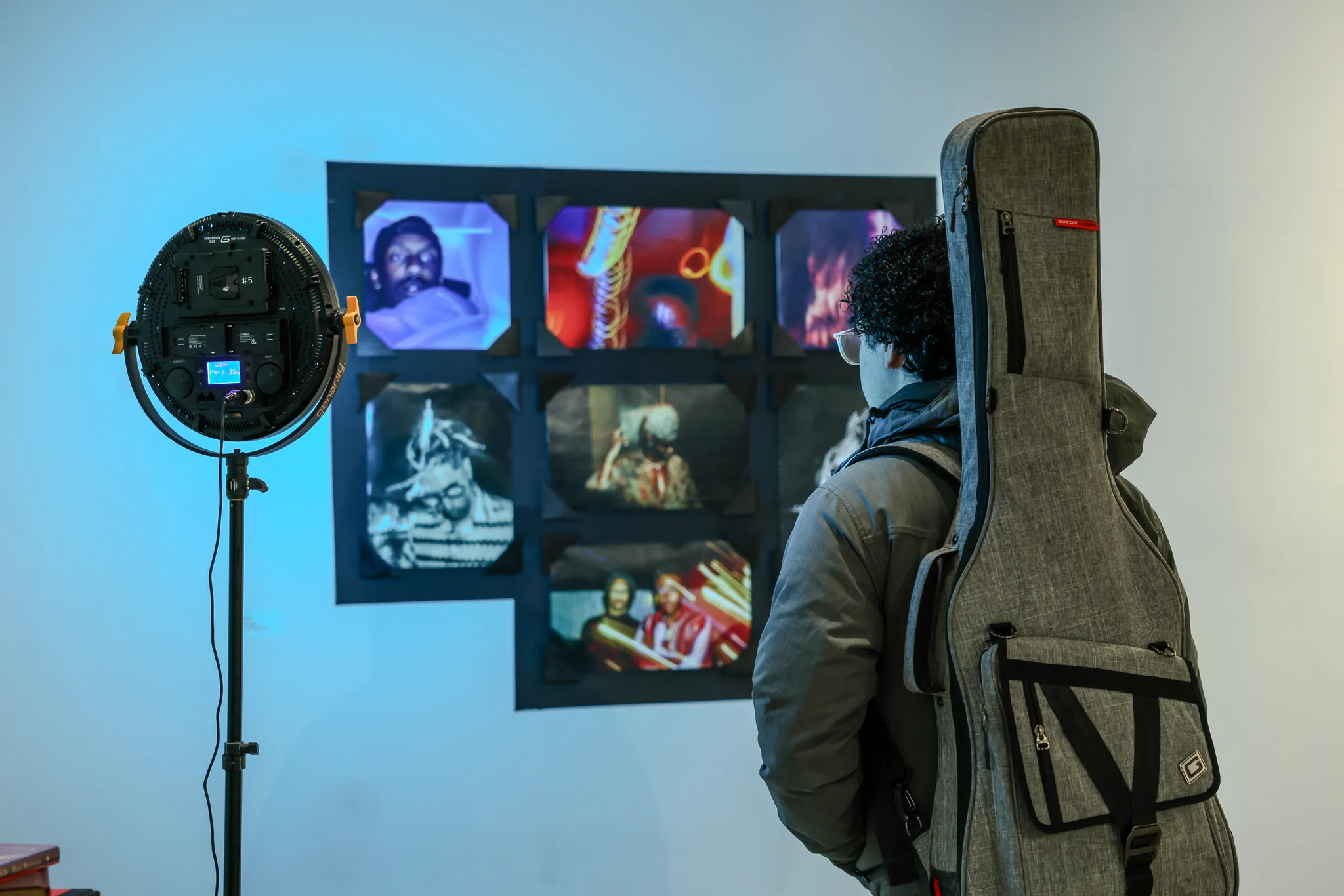 A gallery visitor examines a grid of framed video stills lit by a production light at Future Legends